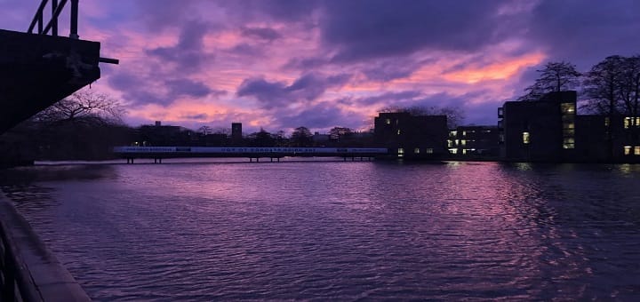 Un atardecer morado sobre un río, capturando el estado de ánimo melancólico y oscuro del poema 'Morado'.